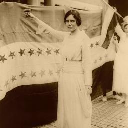 Alice Paul stands in front of flag.