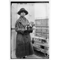 Black and white photograph of Mabel Ping Hua Lee wearing a decorative hat, a button up coat, and holding flowers.