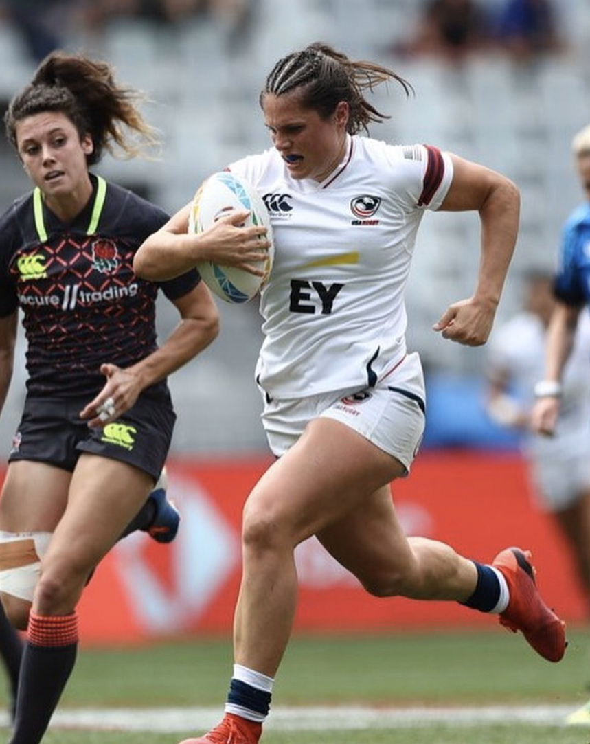 Woman in a white rugby uniform plays against a fellow competitor in a black rugby uniform