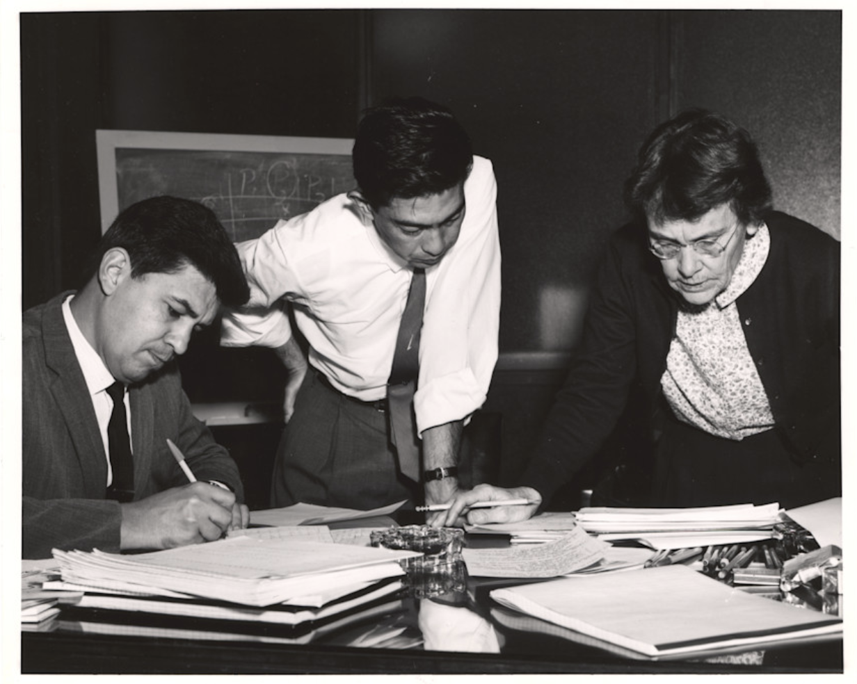 A woman, Barbara McClintock, stands with two other men reviewing notes
