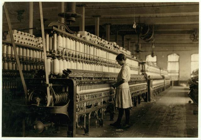 Black and white photo of a small girl working in a cotton gin.