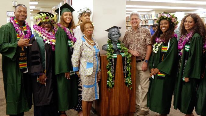 A group of graduates from the University of Hawai'i pose beside a bust of Alice Ball