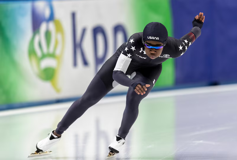 Erin Jackson skating on ice rink wearing all black Team USA uniform.