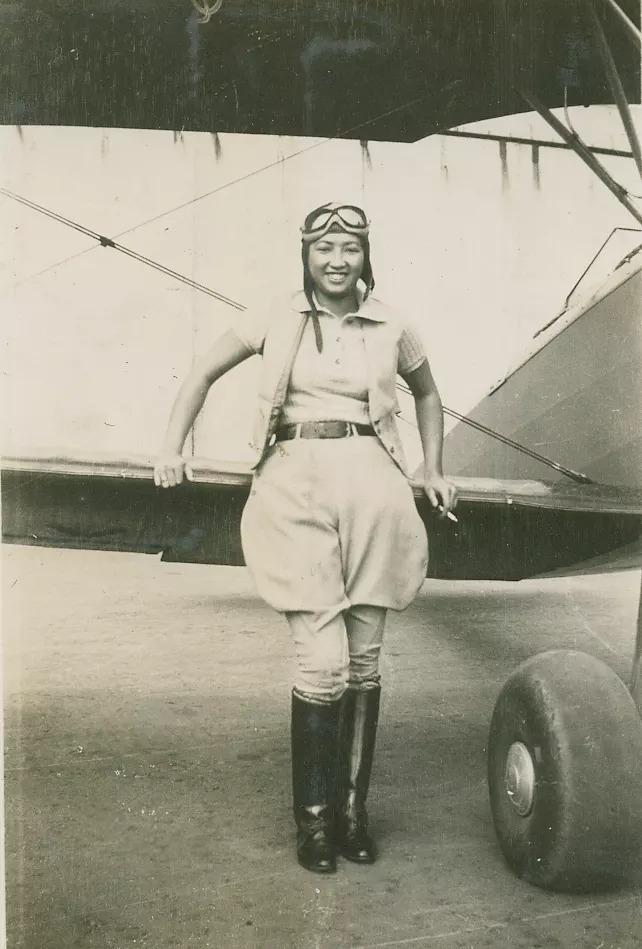 Black and white photo of Hazel Ying Lee standing and smiling in front of a plane.