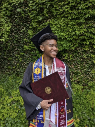 Kihana Wilson stands smiling in graduation regalia for a photo