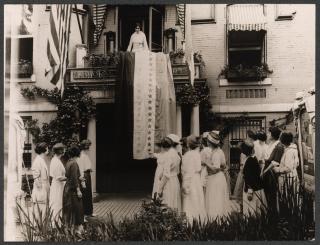 Woman on balcony talks to crowd of women below.