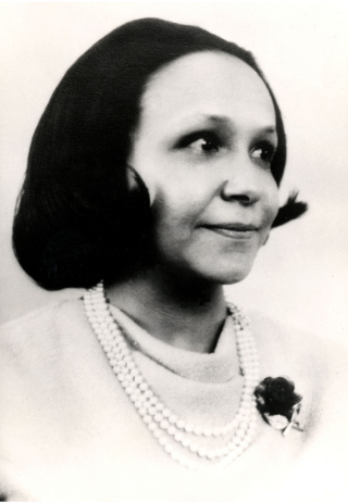 Black and white photo of Cooke Wright sitting for a portrait with short hair and wearing three strings of pearls.