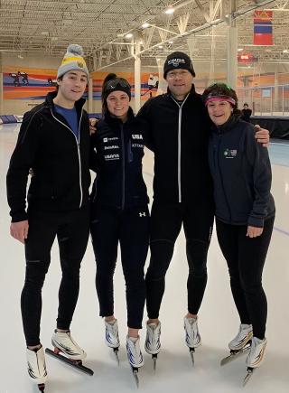 Photo of Bonnie Blair (on the right) with her family, including her husband and two children, on the ice rink. They are all wearing dark skating outfits.