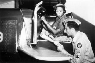 Black and white photo of Hazel Ying Lee in the cockpit of a plane. She is being trained by a man in uniform reading a manual.