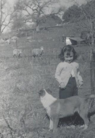 Black and white photo of Peggy Fleming as a child, standing with a dog and smiling at the camera
