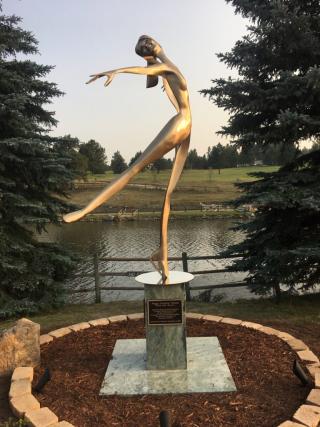 Photo of Peggy Fleming Tribute, a large bronze sculpture posed as if it is skating. There is a pond and nature in the background.