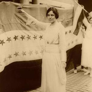 Alice Paul stands in front of flag.