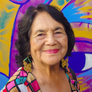Headshot of Dolores Huerta smiling wearing brightly colored shirt in front of brightly colored background.