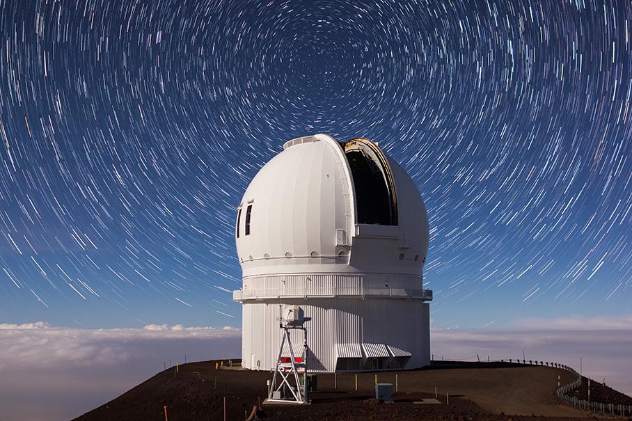 Photo of Maunakea Observatory in Hawai'i. It is a large white structure on top of a mountain. The sky is starry.