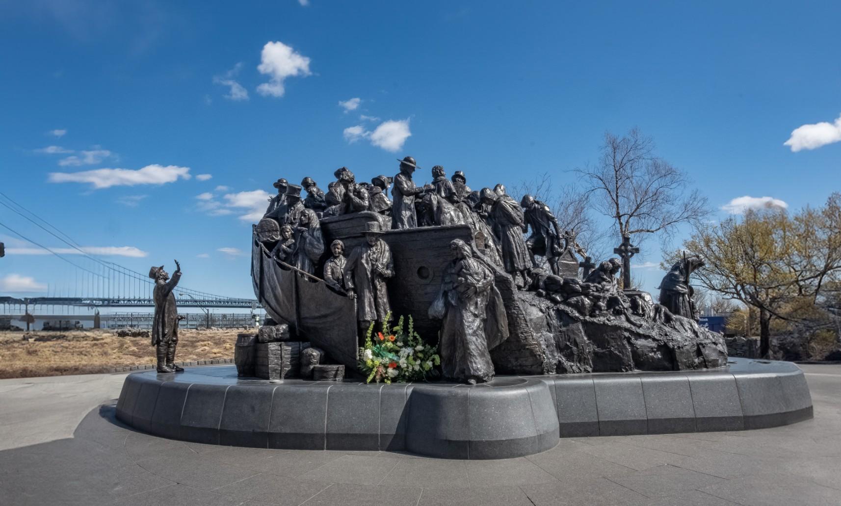 Photo of Irish Memorial created by Glenna Goodacre. It depicts many people struggling on the hull of a boat, and one individual on the ground looking at the boat. It represents the struggle of the Irish Potato Famine and the mass migration of Irish individuals to the United States.