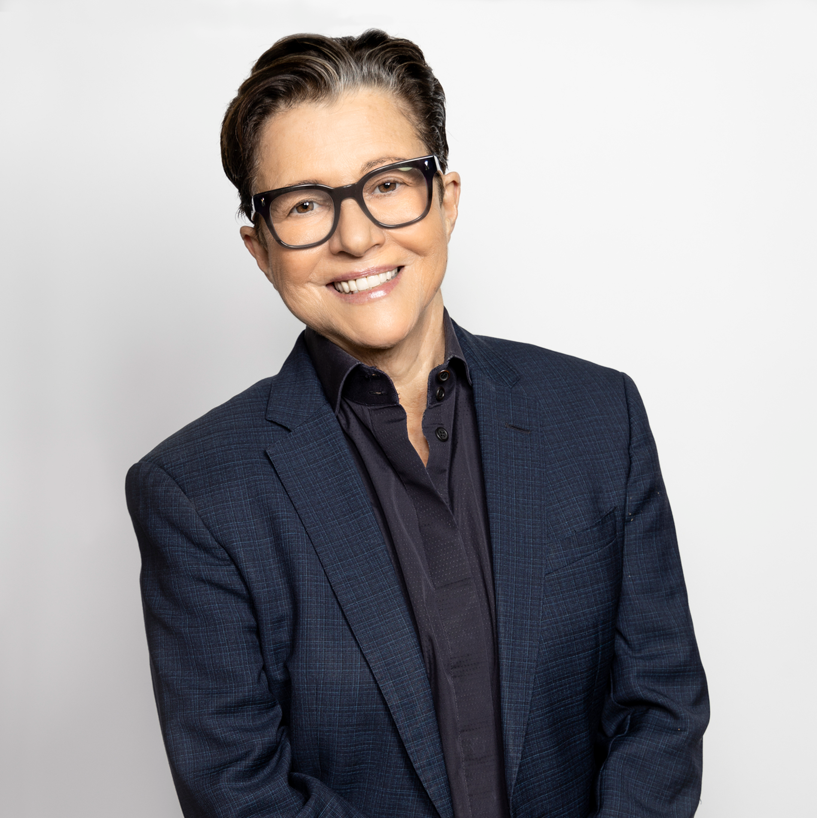 Tena Clarke wearing a navy jacket against a white background, smiling.